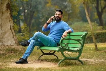 Fototapeta premium Young indian man talking on smartphone at park.