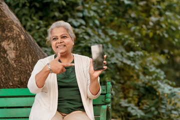 Indian senior woman showing smartphone screen at park