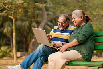 Fototapeta na wymiar indian senior couple sitting at park and using laptop