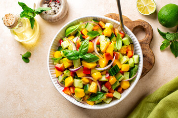 Top view of summer mango salad made with red bell pepper, cucumber, red onion, fresh mint, basil and lime, olive oil and honey dressing. Copy space.