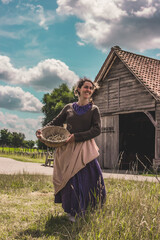 Farmer in front of an old and traditional barn with a basket filled with wheat. Women wearing a traditional costum.