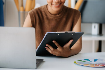 Calm curly brunette dark skinned woman on desk in office of fashion designer and holds tablet and smartphone...