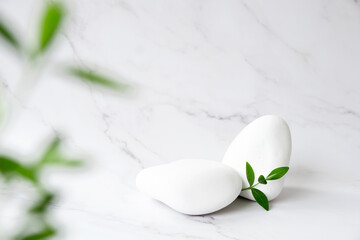 SPA background concept. White stones and and frame of green leaves in defocus on marble background with copy space. Body care and beauty treatment. Spa and wellness or beauty salon concept. Copy space
