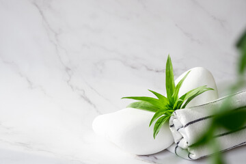 SPA background concept. White stones, towel, and leaves of green plant on marble background with copy space. Body care and beauty treatment. Spa and wellness or massage salon concept. Copy space.