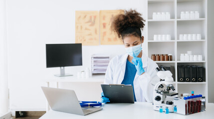 .Young scientists conducting research investigations in a medical laboratory, a researcher in the foreground is using a microscope in laboratory for medicine.