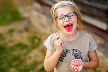 Little adorable preschool girl with eyeglasses eating berry and watermelon ice cream sundae in cup on sunny summer day. Happy child eat icecream dessert. Sweet food on hot warm summertime days