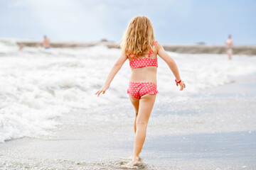 Happy Child, Little Preschool Girl in Swimmsuit Running And Jumping In The Waves During Summer...