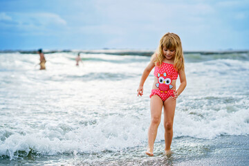 Happy Child, Little Preschool Girl in Swimmsuit Running And Jumping In The Waves During Summer Vacation On Exotic Tropical Beach. Family Journey On Ocean Coast.