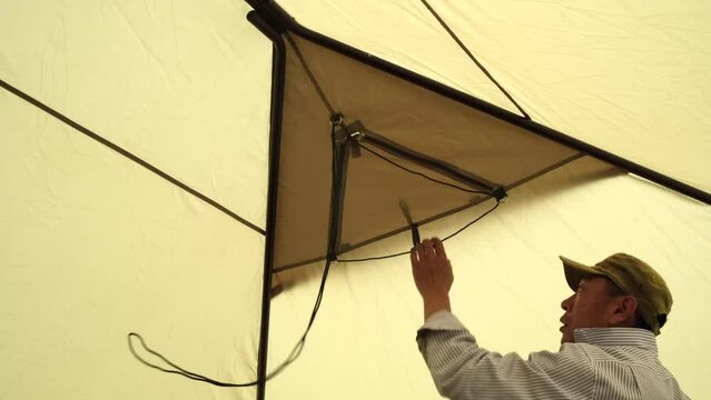 A man opens a triangular window in the roof of the tent inside