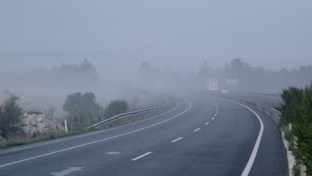 Izmir, Turkey - April 23, 2023: An early morning shot creating a dramatic scene right out of a movie. The picture captures a winding road shrouded in thick mist, creating a low visibility atmosphere. 