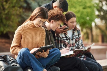 Fototapeta na wymiar Sitting, reading educational material. Four young students in casual clothes are together outdoors