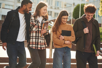 Front view. Four young students in casual clothes are together outdoors