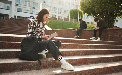 Young female student is sitting on the stairs of university