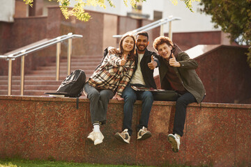 Three young students in casual clothes are together outdoors