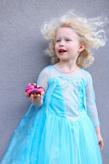 Cute little girl holding pink donut on grey background 