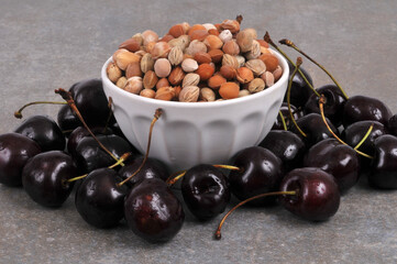 Noyaux de cerises dans un bol avec des cerises autour en gros plan sur fond gris