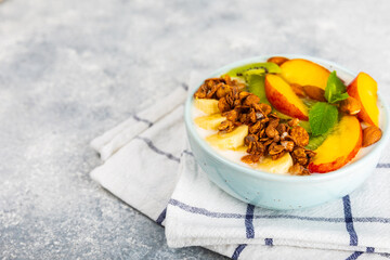Bowl of granola with yogurt and fresh berries on a texture table. Yogurt berries, acai bowl, spirulina bowl. Healthy food, balanced breakfast. Strawberries, blueberries, kiwi, peach, almonds and chia.