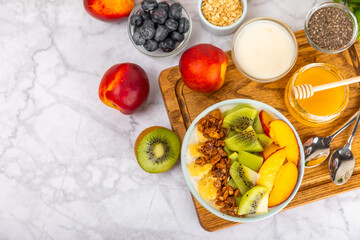 Bowl of granola with yogurt and fresh berries on a texture table. Yogurt berries, acai bowl, spirulina bowl. Healthy food, balanced breakfast. Strawberries, blueberries, kiwi, peach, almonds and chia.
