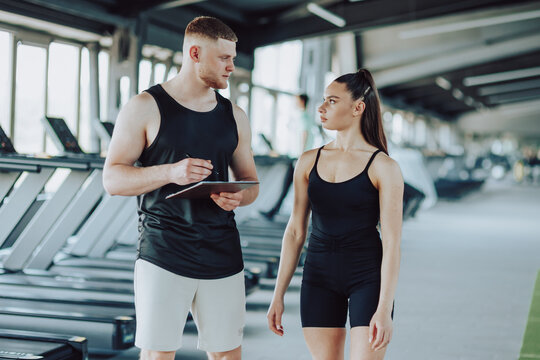 The interaction between a male personal trainer and a woman takes center stage in this image, as they engage in a dynamic dialogue, discussing exercises, and addressing fitness-related questions.
