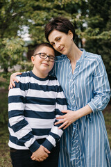 Obraz premium Mom with teenage son are walking in the park. They look at each other and smile. A woman hugs boy and straightens her hair. The concept of mother's day, relationships with adolescents, care and love.