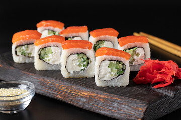 Rolls with salmon and philadelphia cheese on wooden board on black background. Closeup