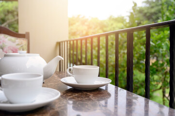 White teapot and cup of tea on table. Outdoor breakfast on balcony cafe.