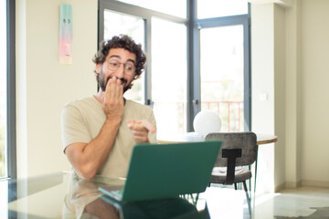 Fototapeta premium young adult bearded man with a laptop laughing at you, pointing to camera and making fun of or mocking you