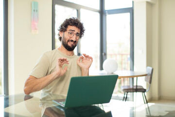 young adult bearded man with a laptop feeling disgusted and irritated, sticking tongue out, disliking something nasty and yucky