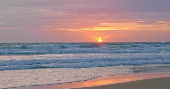 The sun is setting over the horizon and the waves of the sea are crashing towards the shore..Bright clouds as the sun sets over the horizon and waves of the sea come to shore..