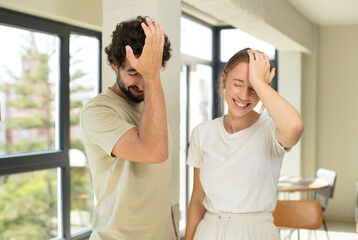 young adult couple laughing and slapping forehead like saying d’oh! I forgot or that was a stupid...
