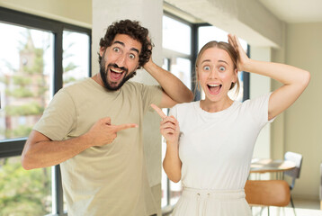 young adult couple laughing, looking happy, positive and surprised, realizing a great idea pointing to lateral copy space