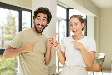 Obraz premium young adult couple feeling joyful and surprised, smiling with a shocked expression and pointing to the side