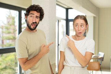 Fototapeta premium young adult couple feeling joyful and surprised, smiling with a shocked expression and pointing to the side