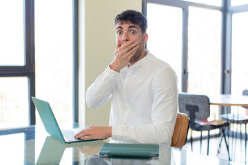 young handsome man covering mouth with a hand and shocked or surprised expression. working at home concept