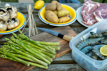 Various vegetables - asparagus, mushrooms, potatoes and meat - pork and shrimp on wooden table. Preparing for barbecue.