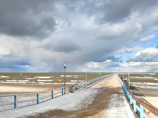 Winter beach with snow clouds and blue sky in day time Palanga bridge
