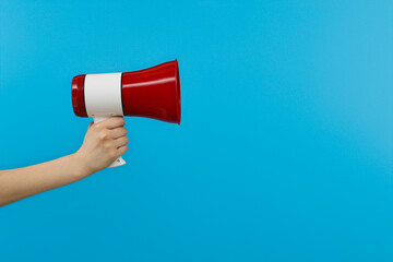 Red bullhorn in hand on blue background, space for text