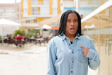 afro pretty black woman looking shocked and surprised with mouth wide open, pointing to self