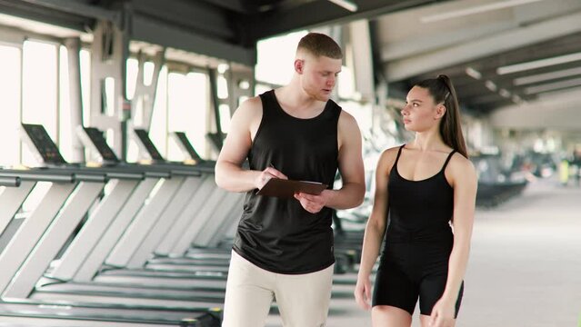 The interaction between a male personal trainer and a woman takes center stage in this image, as they engage in a dynamic dialogue, discussing exercises, and addressing fitness-related questions.