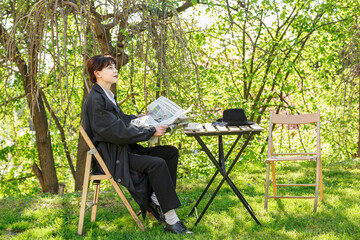 A beautiful girl drinks coffee at the table, in a raincoat, in a white shirt, in black trousers with suspenders