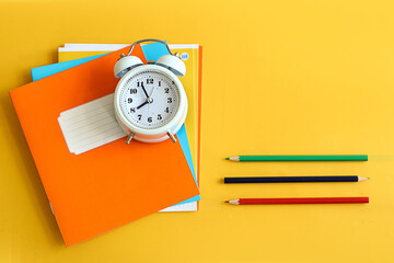 Back to school: school supplies, alarm clock on yellow background, space for text, top view