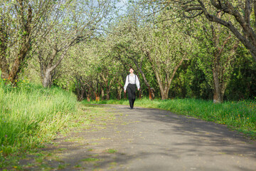 A beautiful girl in a white shirt, in black trousers with suspenders against the background of the sky and green grass