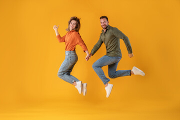 Fototapeta na wymiar Excited young european spouses running, jumping, freeze in air and smiling at camera, isolated on yellow background, full length. Fun together, offer and ad, sale