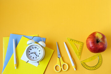 Back to school: school supplies, red apple, alarm clock on yellow background, space for text, top...