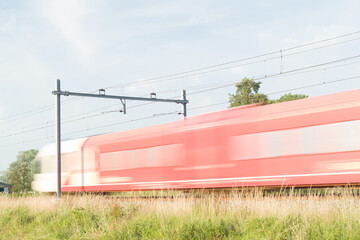 Red and white train rushes by at high speed, blurred by long exposure in Arnhem in the Netherlands