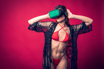Studio photo shoot of beautiful brown hair model posing wearing red swimwear and vr glasses with...