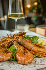 Langoustine with lemon and wine. Seafood close up. Fish dish with glass of wine. Fish restaurant menu. Grilled scampi with salad. Mediterranean mollusk plate. Flat lay photo. Roasted shrimps.