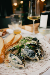 Mussels in cream sauce with bread and wine. Seafood close up. Fish dish with glass of wine. Fish restaurant menu. Fried mussels with shells in sauce. Mediterranean mollusk plate. Flat lay photo. 