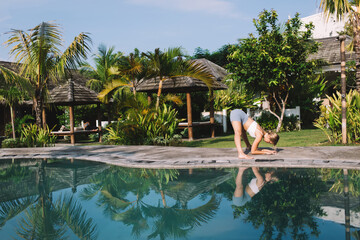 Slim woman doing Prasarita Padottanasana yoga on poolside