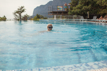 Beautiful old woman in pool against sea. Senior woman dressed swimsuit and enjoy swim in the pool...